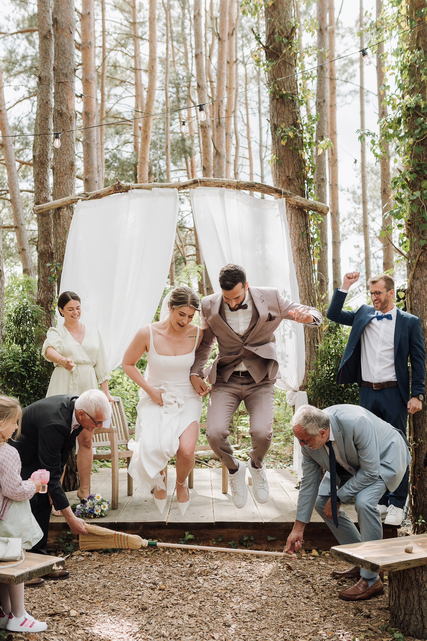 Hochzeit Framhouse Wandlitz, Freie Trauung, Hochzeitsfotografin Berlin, Emotionale ;Momente, Authentische Hochzeitsfotografie, Brautpaar springt über Besen, Ritual